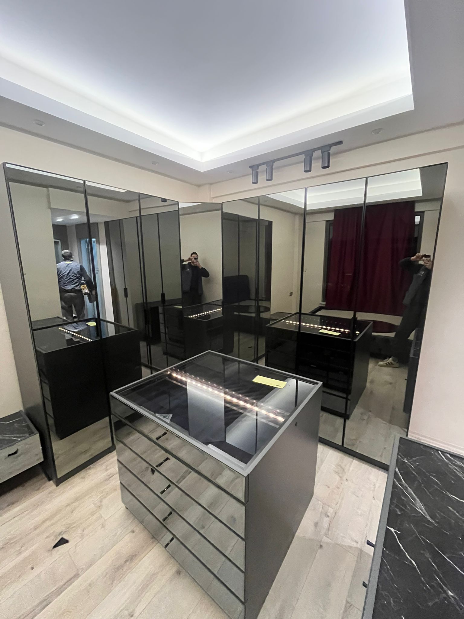A modern walk-in closet featuring elegant mirrored wardrobes and a central island unit with illuminated glass-top drawers. Premium inegol furniture design.
