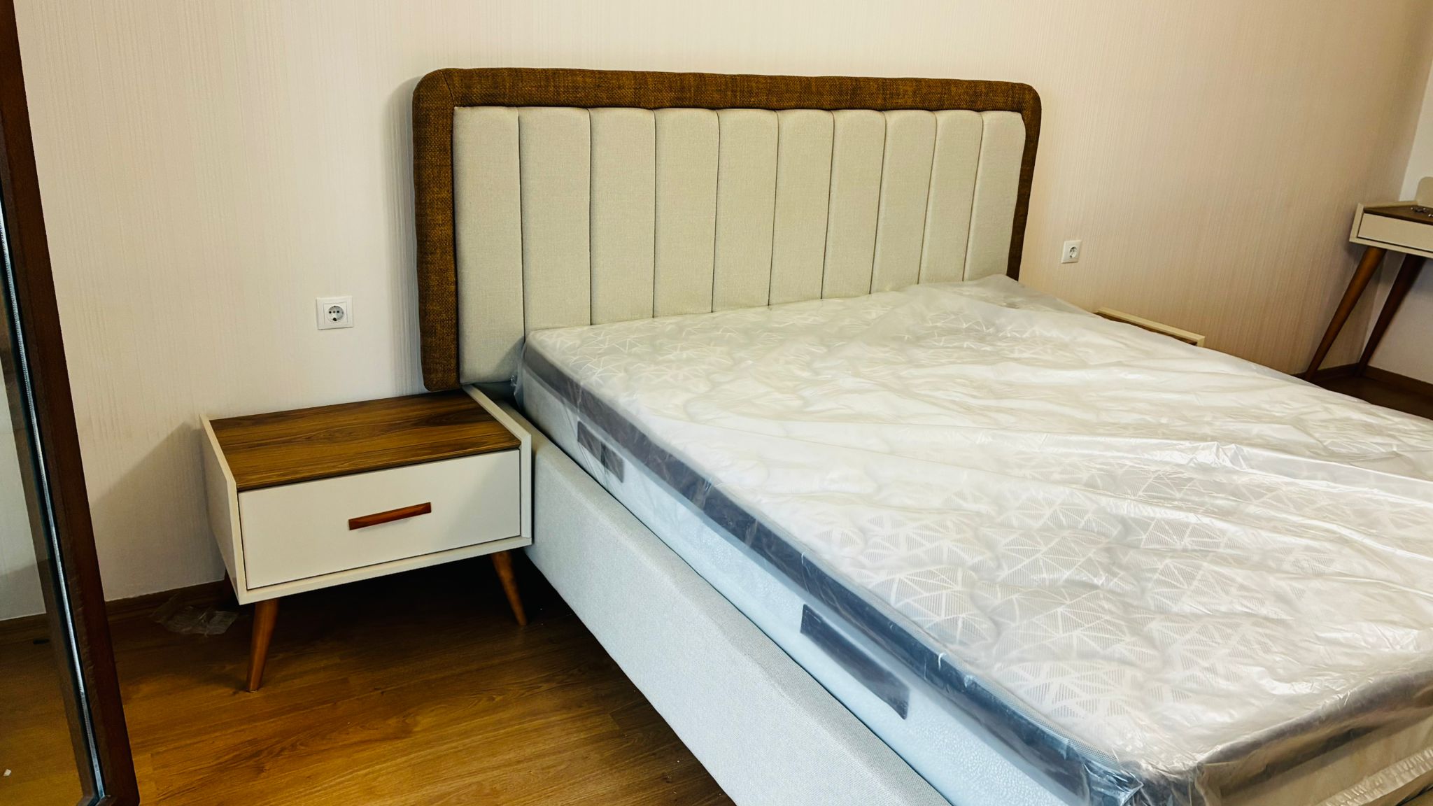 A modern bedroom set featuring an upholstered beige headboard, white bed base, and wooden-top nightstands, showcasing elegant Inegol furniture design.