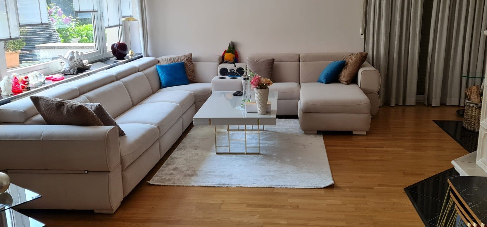 A chic living room decorated with a spacious, comfortable light beige modern sectional sofa. This Modern Inegol furniture is complemented by wooden flooring and a white rug.