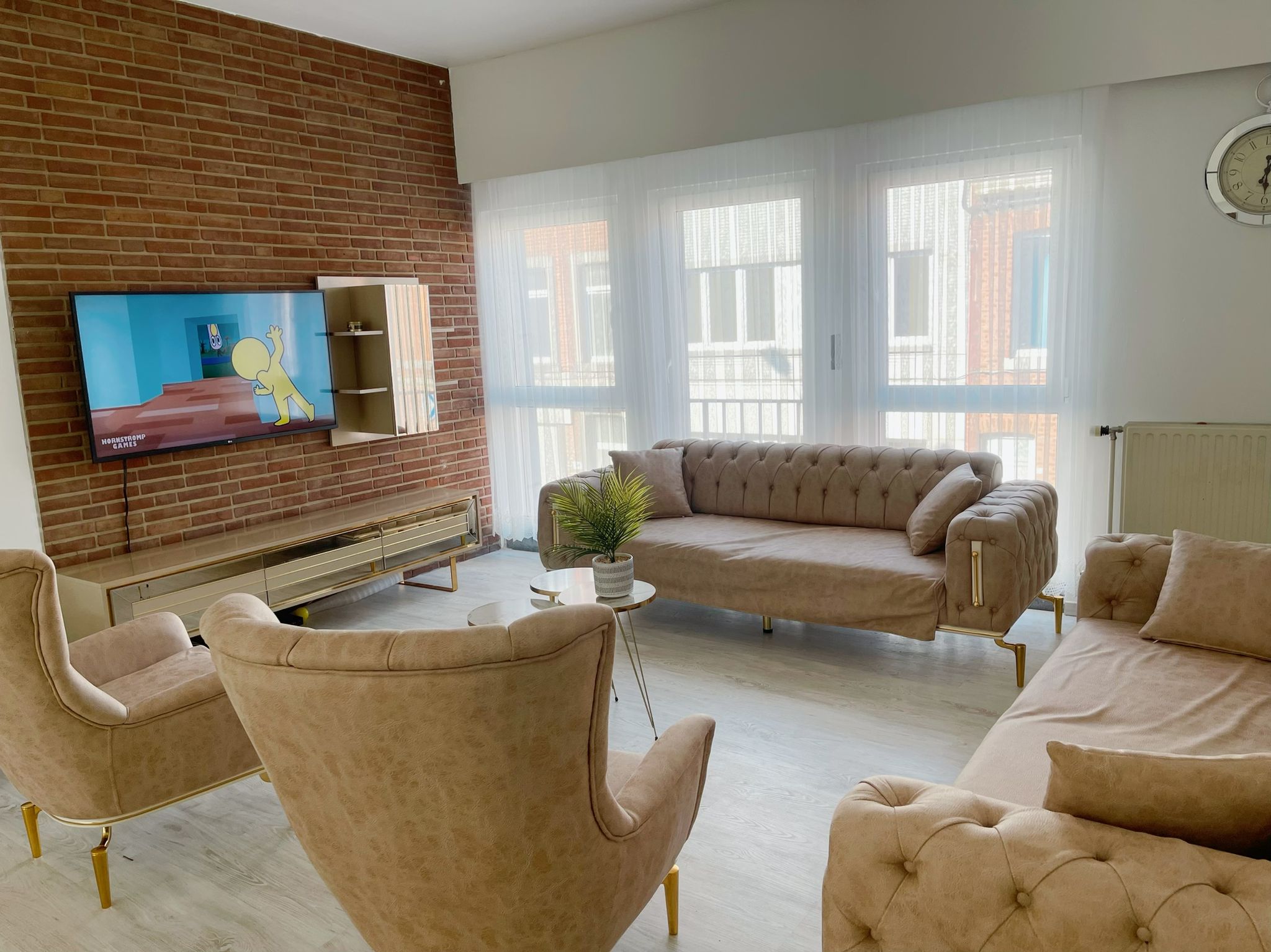 Modern living room featuring a beige Chesterfield sofa set, brick wall, and TV unit. Discover comfort with Inegol furniture campaigns.