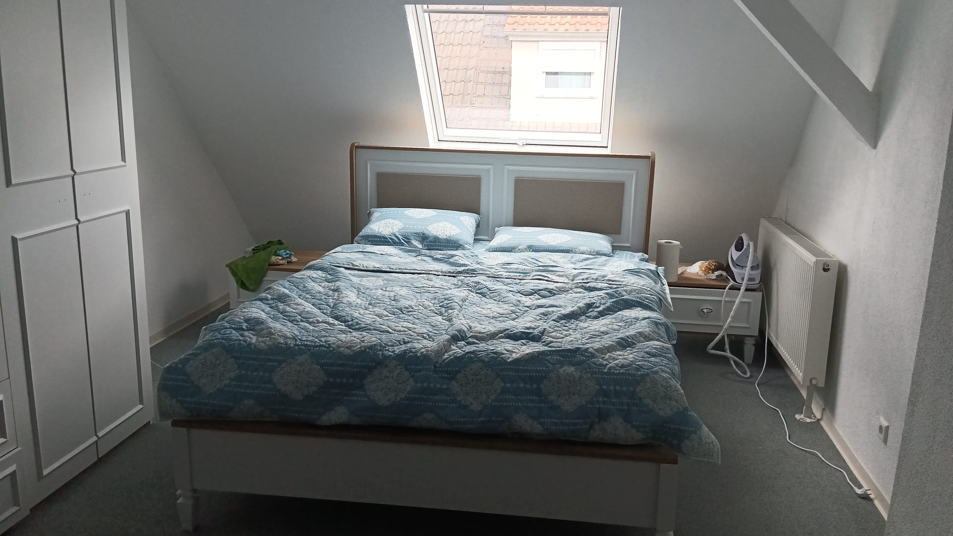 Cozy attic bedroom with an elegant white headboard bed, blue patterned bedding, and a spacious white wardrobe. Modern Inegol furniture designs.