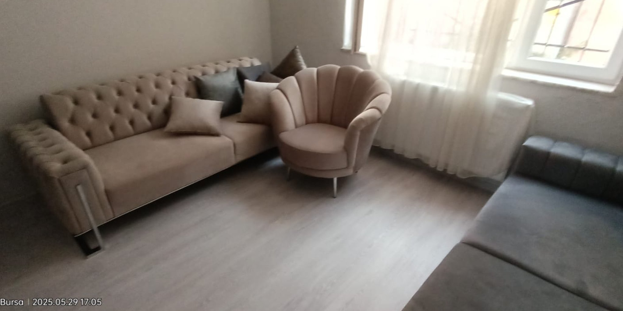 Modern living room featuring a beige chesterfield corner sofa and a distinctive shell-design armchair on light wooden flooring. Quality inegol furniture.