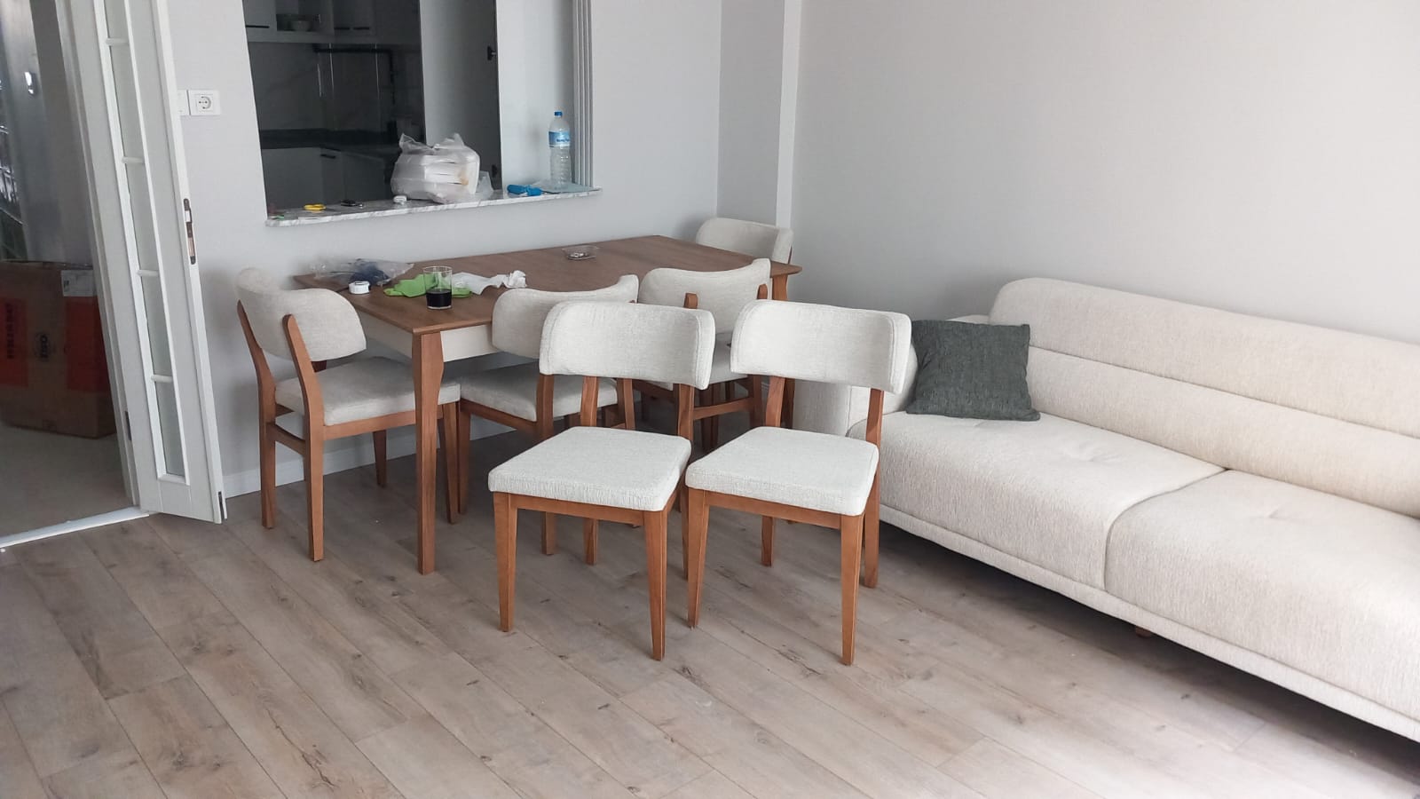A stylish dining room set featuring a light wooden table and modern cream upholstered chairs, complemented by a minimalist sofa, reflecting Inegol furniture models.