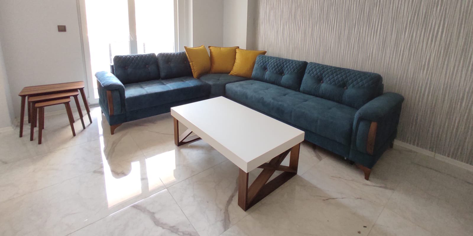 Elegant living room set featuring a dark teal corner sofa, white coffee table, and nesting side tables. Experience Quality Inegol furniture comfort.