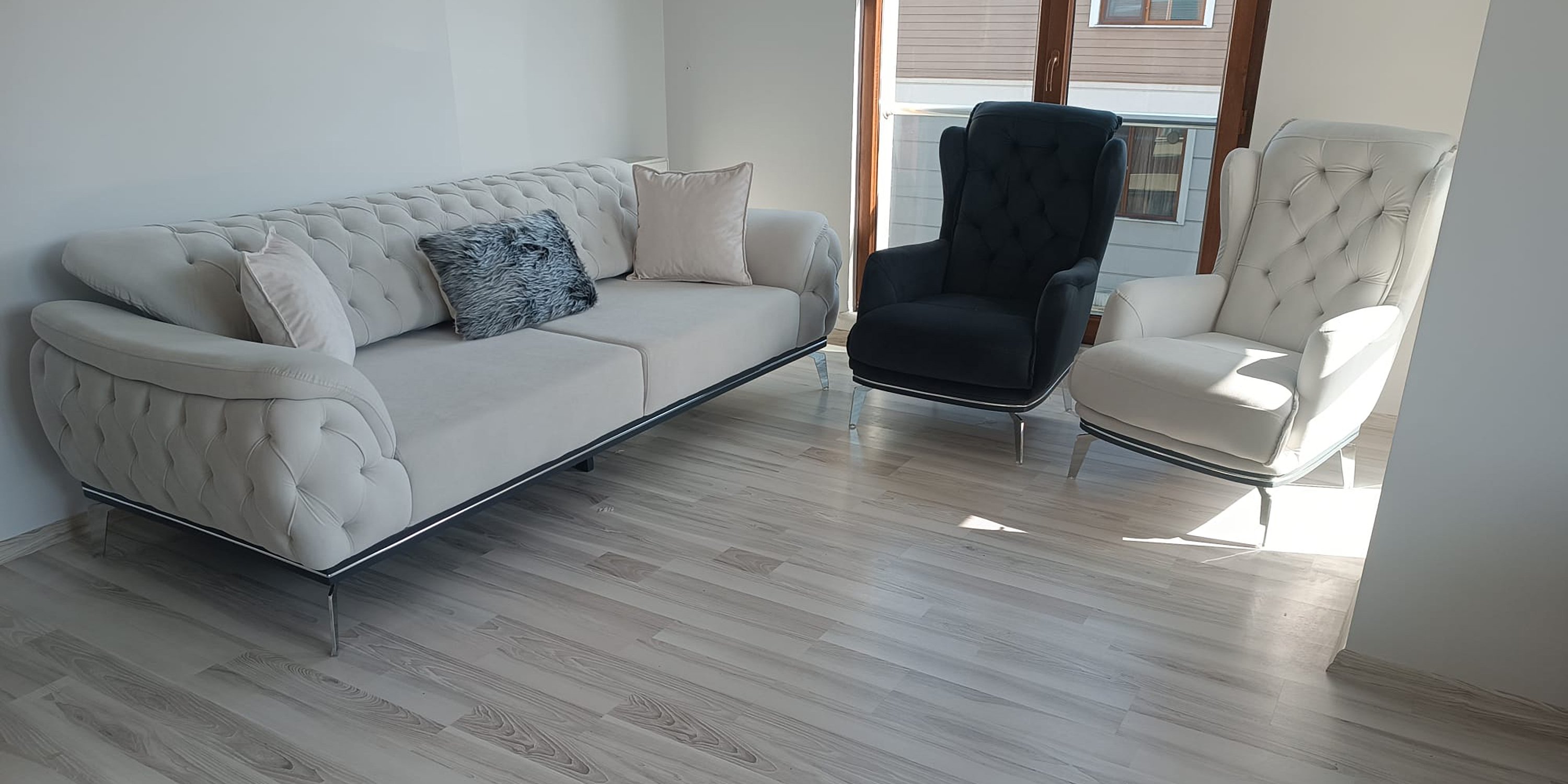 A stylish modern beige tufted sofa set with elegant chrome legs. Accompanied by one black and one cream wingback armchair. Modern Inegol furniture.