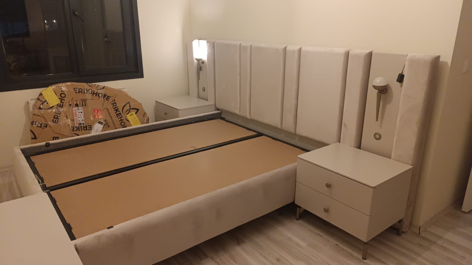 Modern bedroom set featuring a tall, paneled beige upholstered headboard with integrated lights and two matching nightstands. This elegant Inegol furniture piece combines comfort and style.