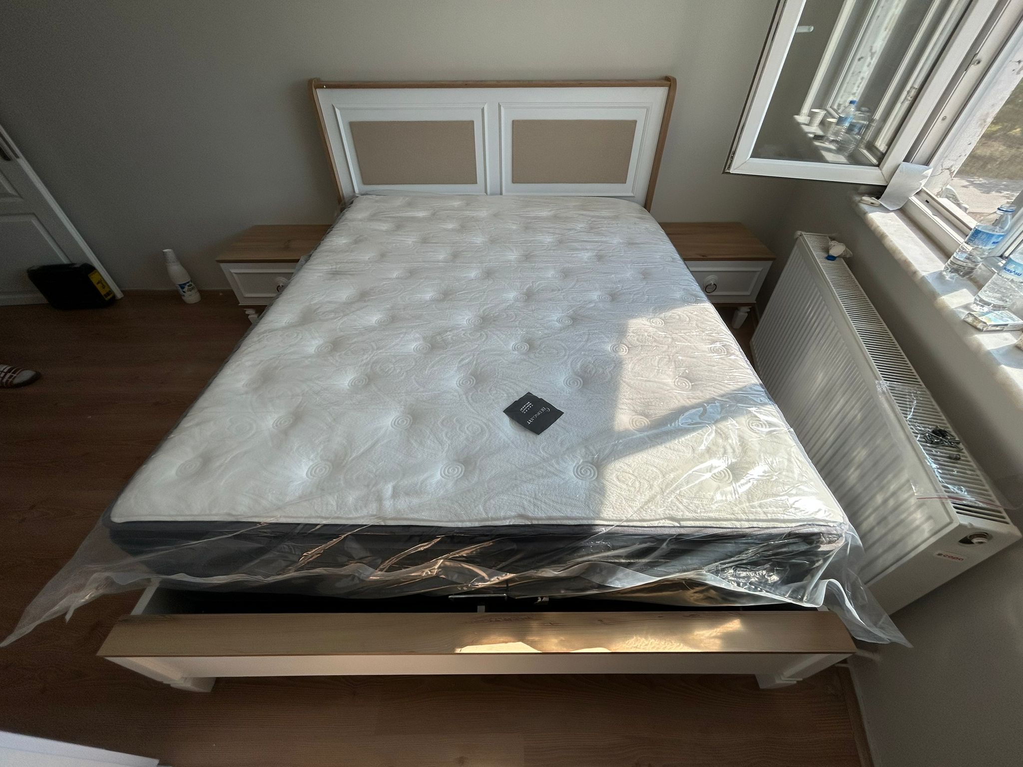 Modern bedroom setup featuring a new packaged mattress, a wooden and white headboard, and side tables from İnegöl furniture.