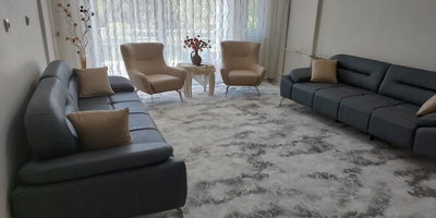 Gri modern İnegöl mobilya koltuk takımı, bej berjerler, mermer desenli halı ve şık aksesuarlarla donatılmış ferah bir oturma odası.