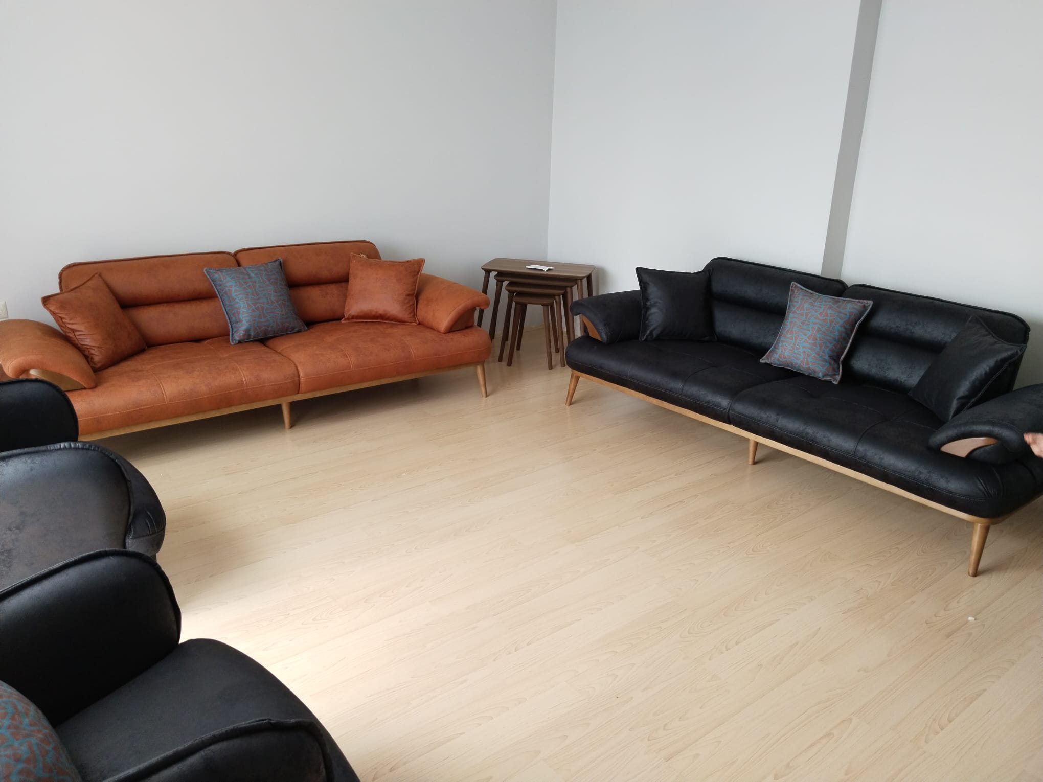 A living room furnished with modern brown and black sofas with light wooden legs, matching cushions, and stylish Inegol furniture models including nesting tables.