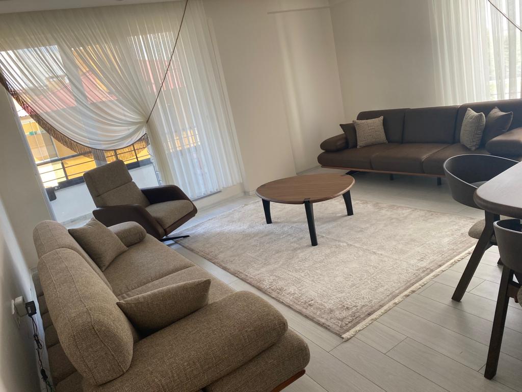 Spacious modern living room featuring brown and beige sofas, a wooden coffee table, and a comfortable recliner chair. Showcases stylish Inegol furniture models.
