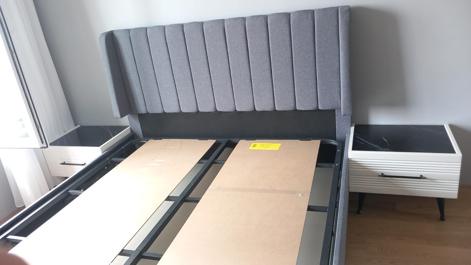 Modern and stylish grey fabric vertically tufted headboard bed base, complemented by white nightstands with black marble-look tops. A high-quality Inegol furniture product.