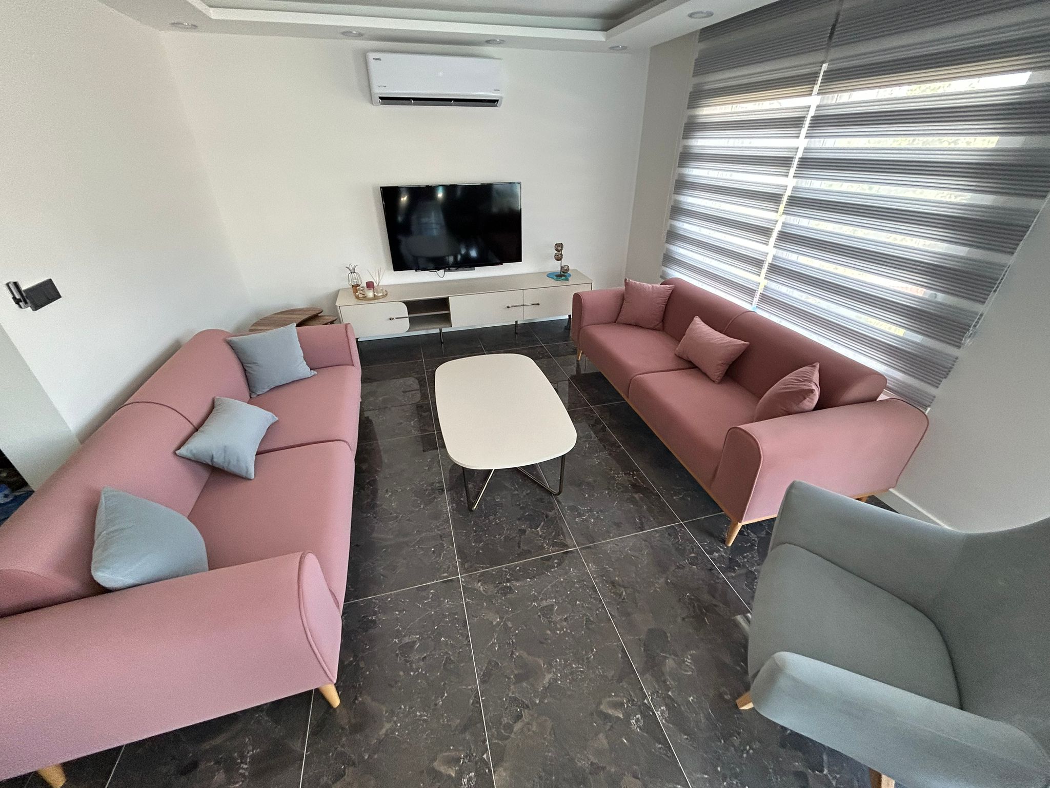 Füsun Ertaş - Muğla modern living room set featuring pink two and three-seater sofas, a grey armchair, and contemporary decor. Affordable Inegol Furniture.