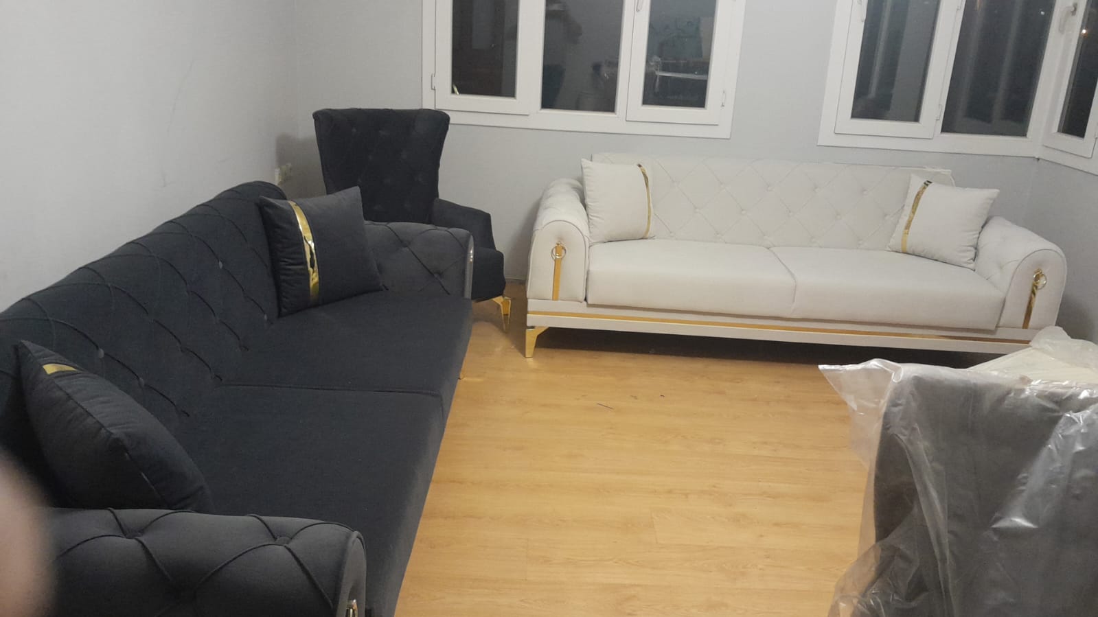 A modern living room set featuring dark gray and cream sofas with elegant gold accents. The Hakan Altınok - Adana collection highlights modern Inegol furniture style.
