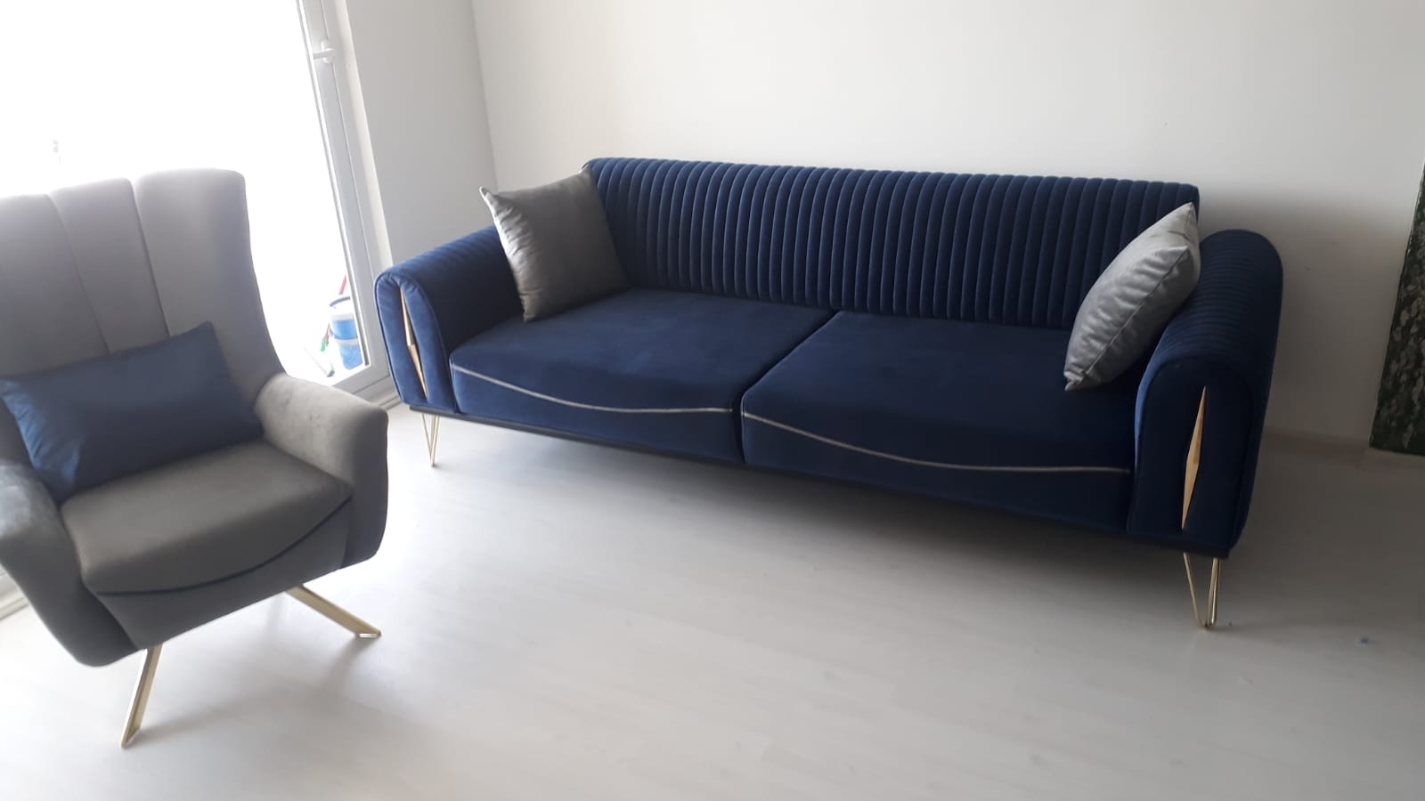Modern navy blue velvet triple sofa and grey armchair. This elegant furniture set with chic gold legs and details enhances any living space.