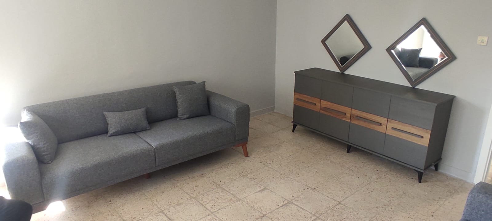 Contemporary grey three-seater sofa with wooden detailed sideboard and diamond-shaped mirrors. Offers elegant inegol furniture design for living rooms.