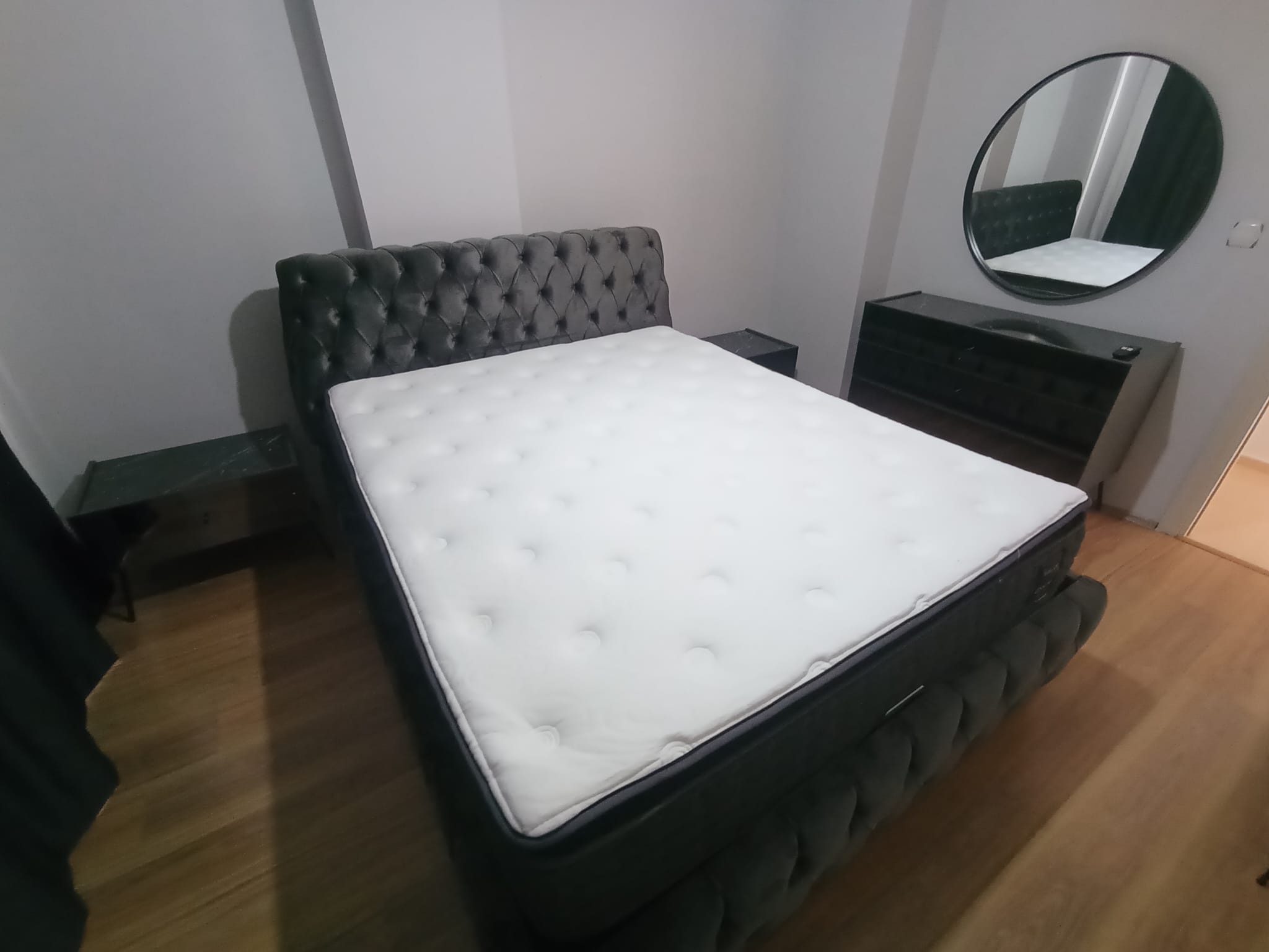 Modern dark gray upholstered bed with a comfortable mattress, two nightstands, a dresser, and a round mirror. Quality Inegol furniture.