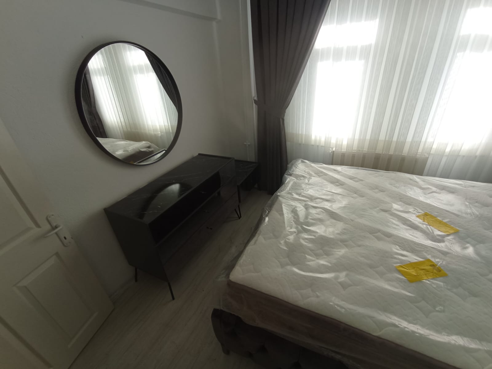 Modern bedroom in a new home featuring a black marble pattern dresser, round mirror, and a new bed. Excellent value for Inegol furniture prices.