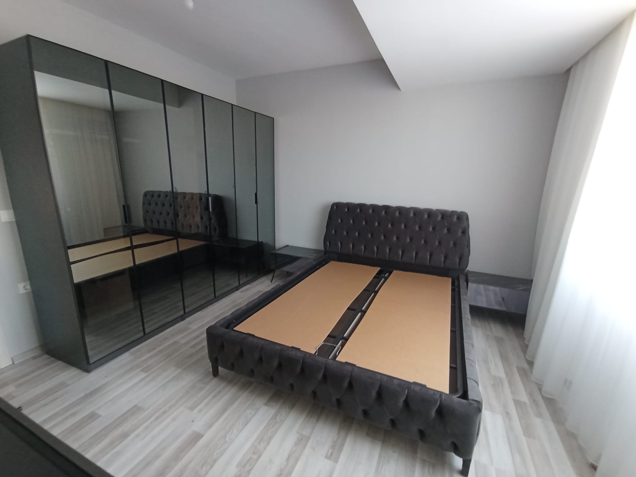 Modern dark grey velvet upholstered bed and mirrored wardrobe form an elegant bedroom set. High-Quality Inegol Furniture adds sophistication.