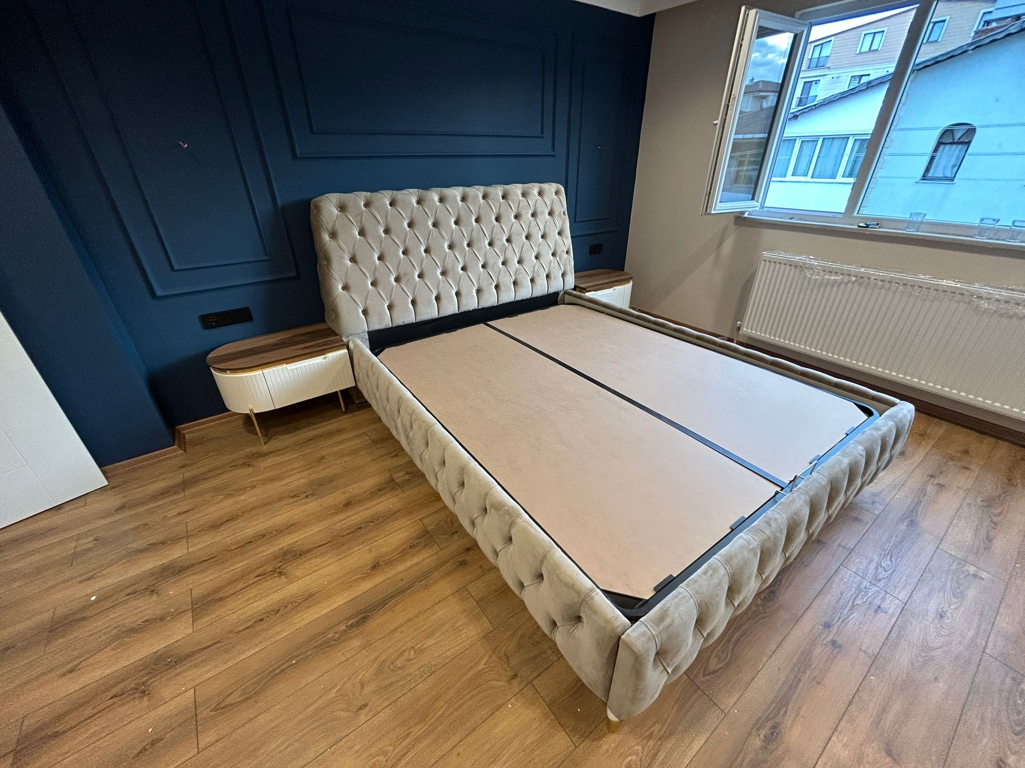 Elegant beige tufted bed frame in a modern bedroom with navy wall paneling and wooden floor. Discover competitive Inegol furniture prices.