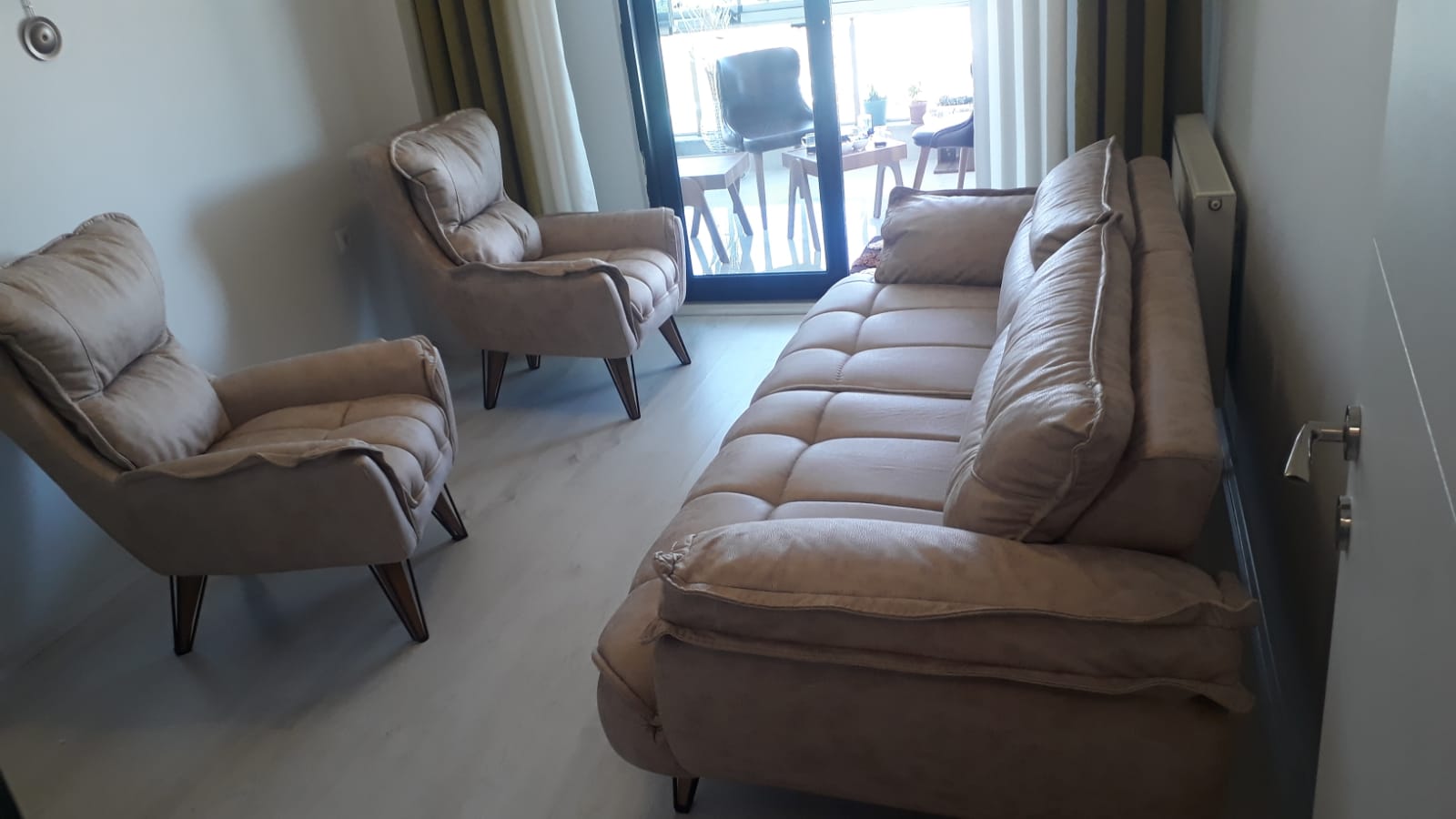 Elegant living room set featuring a beige three-seater sofa and two armchairs, in a modern Inegol furniture style, by a balcony.