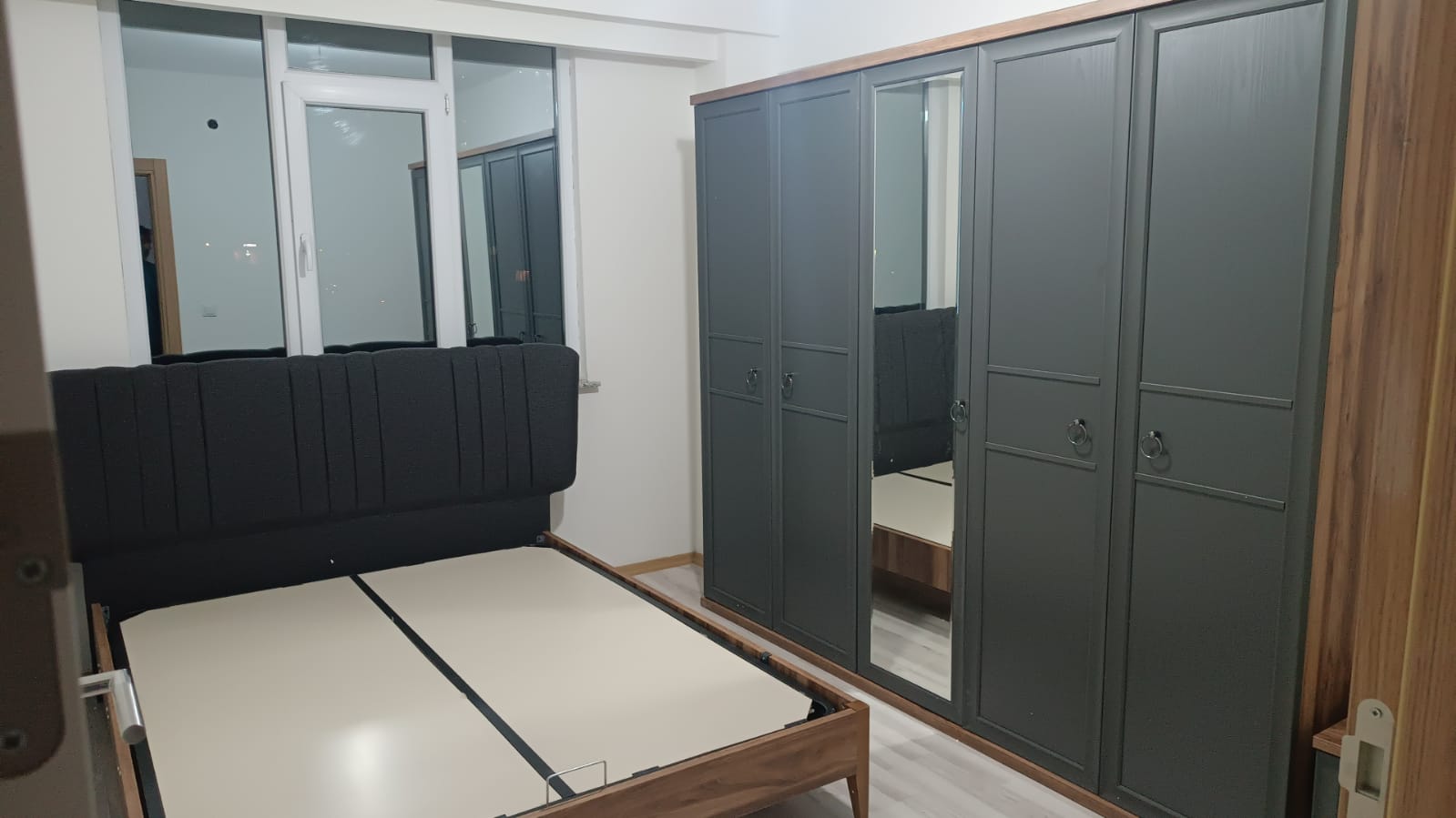 Modern bedroom featuring a dark gray wardrobe with mirrored doors and an upholstered black headboard, Inegol furniture quality.