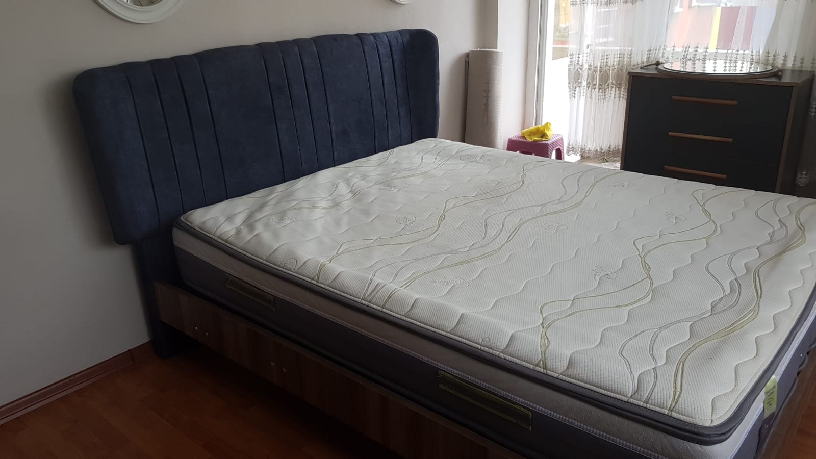 A stylish bed featuring a navy velvet headboard and a high-quality mattress on a wooden base, representing contemporary Inegol furniture models.