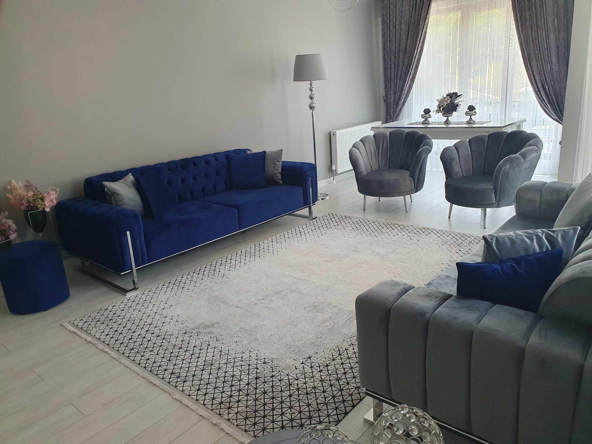 Modern blue velvet sofa set, grey L-couch, stylish accent chairs, and a patterned rug creating an elegant Inegol furniture living room decor.