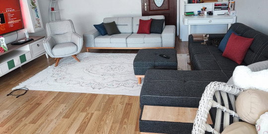 Modern gri koltuk takımı ve L köşe koltuk ile döşenmiş oturma odası. Ahşap detaylı mobilyalar ve açık renk halı. Bursa mobilya şıklığı.
